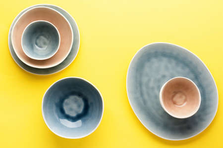 Beautiful blue, grey, beige dinnerware, plates bowls on yellow background table, top view, copy space, selective focusの写真素材
