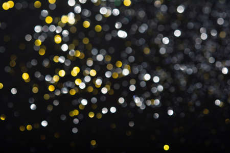 Abstract blurred glitter bokeh background in silver gold, on blackの写真素材