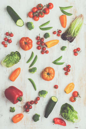 Fresh raw ingredients pattern, for salad tomatoes cucumbers lettuce pepper avocado spring onion broccoli peas on the white wood table, top view, toned, selective focusの写真素材