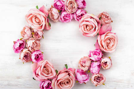 Floral wreath on white wooden table. Artificial roses frame, top view, selective focus