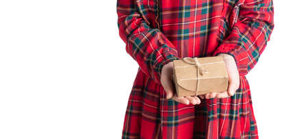Little girls hands holding present in brown craft paper box with jute twine bow. Child in red tartan dress, white background, selective focusの写真素材