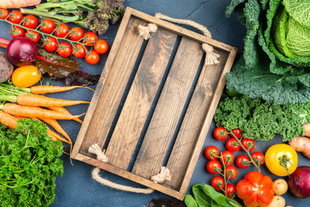 Raw vegan background, Organic vegetables broccoli cauliflower carrots tomatoes kale pak choy onions with wooden box. Healthy local farm produce on blue concrete table, top view, selective focusの写真素材