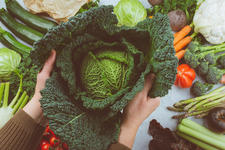 Healthy eating concept. Womans hands holding cabbage. Organic vegetables broccoli cauliflower carrots kale pak choy. Healthy local raw produce on white wooden table, top view, toned, selective focusの写真素材