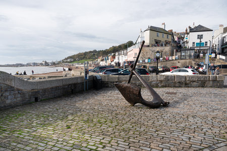 Lyme Regis, United Kingdom - October 29 2022: View of anchor on beach in Dorset, South West, United Kingdom. Car park and town on the back. View of pebbly beach and blue sea, selective focusのeditorial素材