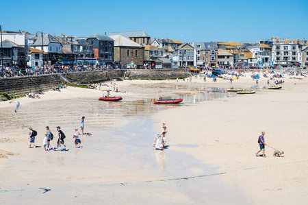 St Ives, United Kingdom - June 3 2022: People on sandy beach in West Cornwall, South West, United Kingdom. View of beach, houses, hotels and boats in low tide. Popular holiday town, selective focusのeditorial素材
