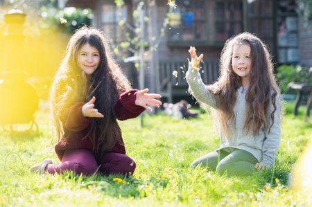 Two little girls with long hair, one brunette, one blonde, playing in the garden on the grass, light flare special effect, selective focusの写真素材