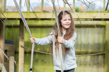 A little girl with long wavy hair swinging on the garden swing in the backyard, green fence on the background, selective focusの写真素材