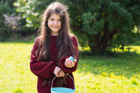 Young girl portrait in the garden, child with long brown hair, dark red jumper standing in front of...