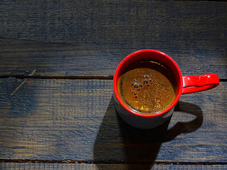 black coffee in a red cup on a wooden surface