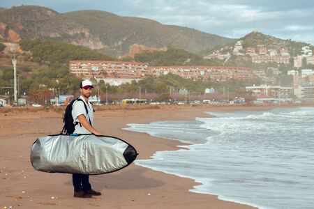 Boy walking along the beach by the sea with cap and surfboardの写真素材