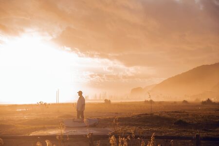 Sunset portrait of surfer boy with cap and surfboard walking on the beachの写真素材