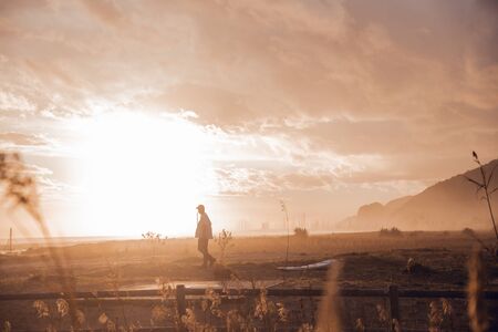 Sunset portrait of surfer boy with cap and surfboard walking on the beachの写真素材