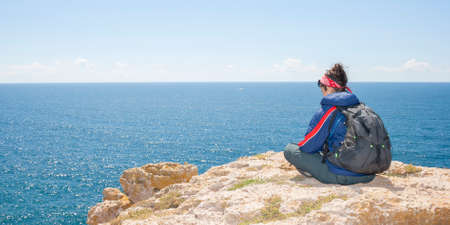 Woman sitting on the cliff in front of the seaの写真素材