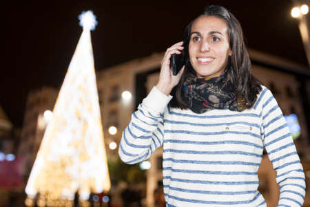 Beautiful woman talking by phone with a christmas backgroundの写真素材