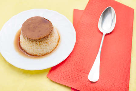Closeup of vanilla flan with caramel red napkins and spoon on yellow tableの写真素材