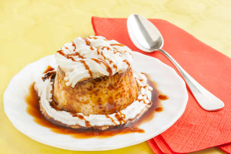Closeup of vanilla flan with cream and caramel with red napkins and spoon on yellow tableの写真素材