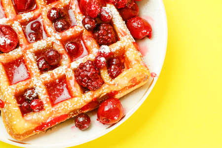 Closeup of delicious waffle with red berries on yellow background