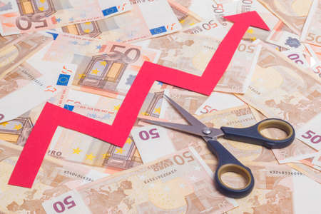 Stop increasing euro value concept. Scissor cutting growing arrow over fifty euro notes backgroundの写真素材
