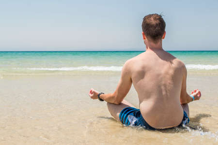 Young adult man meditating at the beachの写真素材