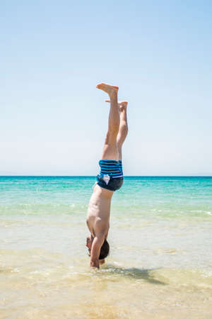 Young adult man handstanding at the beachの写真素材