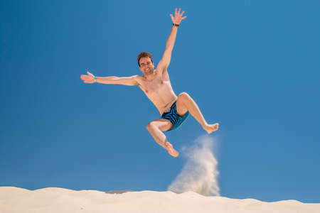 Young adult man jumping at the beach with blue sky backgroundの写真素材