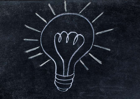 Shiny lightbulb drawn on black chalkboard backgroundの写真素材