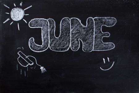 Handwritten June with sun of summer, smile and graduation cap on black chalkboardの写真素材