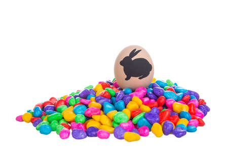 Close-up of decorative egg with painted silhouette of easter bunny on pile of colorful stones....
