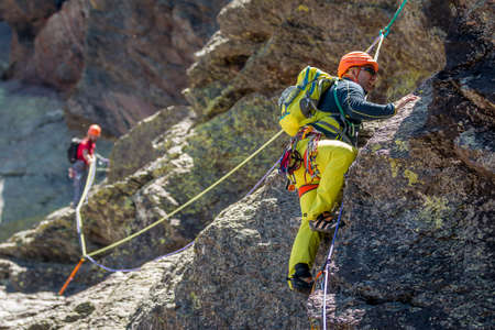 Two extreme men tourists climbing up on mountain in sunny day