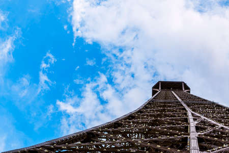 From below metallic Eiffel tower and cloudy blue sky