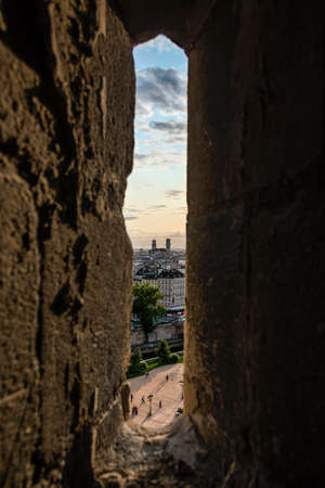 Narrow window in stone wall with view of beautiful Paris cityscape in clouds
