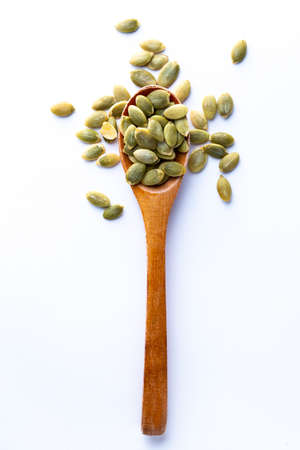 Flat lay of wooden spoon filled with pumpkin seeds lying on white backgrounの写真素材