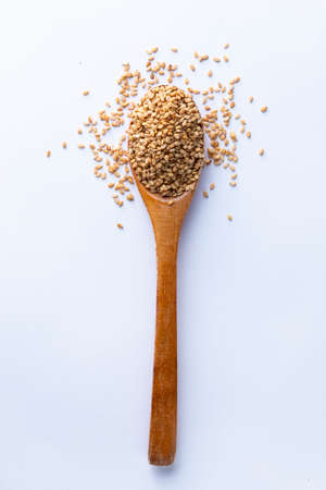 Flat lay of wooden spoon filled with small seeds of sesame lying on white backgrounの写真素材