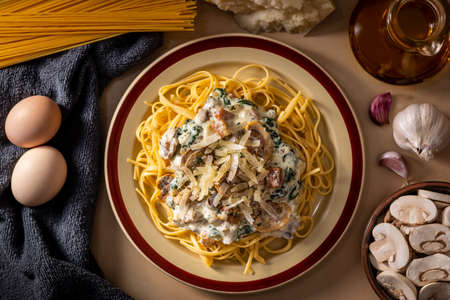 Flat lay of cooked spaghetti with creamy sauce and cheese on top arranged among fresh cooking ingredientsの写真素材