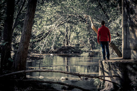 View of man standing on concrete edge in dark park with view of tranquil pond on backgroundの写真素材