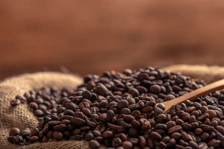 Close-up view of sack of spilled fresh coffee beans with wooden spoon on brown backgroundの写真素材