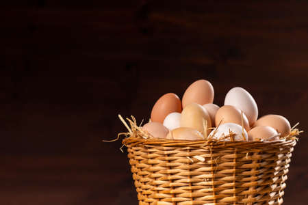Wicker basket with fresh raw eggs on dark backgroundの写真素材