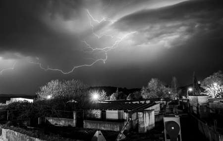 Bright lightningÂ cracking on violet evening sky during thunderstorm over houses of tiny townの写真素材