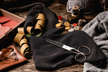 Composition of black polka-dotted fabric with scissors, sewing spools, tape measure and colorful...