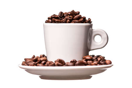 Close-up of white porcelain cup on saucer filled with roasted aromatic coffee beans isolated on...