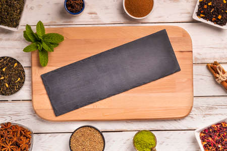 From above frame of different kinds of spice in small plates with slate board in center on wooden...