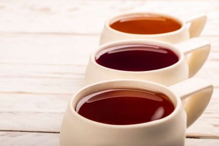 Close-up minimalistic composition of white ceramic mugs with different kind of tea on white wooden...