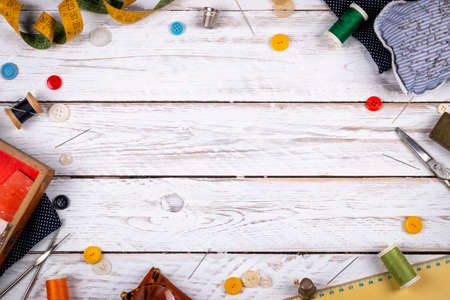 Beautiful set of scattered across white wooden table metal scissors, assorted buttons and sewing spools with colorful threads and tape measure from aboveの写真素材
