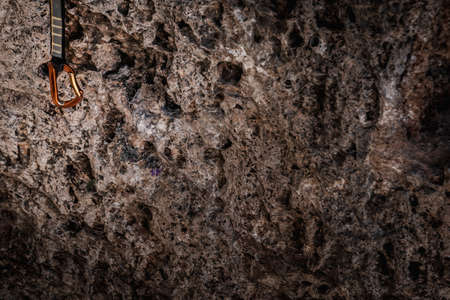 Small shiny metal alpinism carabine on climbing rope hanging on background of rough dark rockの写真素材