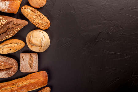 Flat lay of abundance of baked fresh loaves of bread and baguette on black table surfaceの写真素材