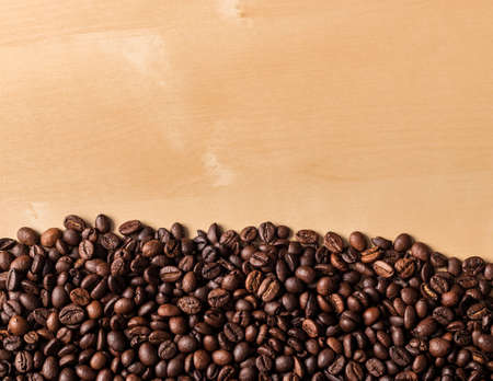 View from above of spilled fresh coffee beans on beige wooden table