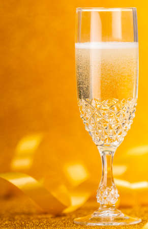 Closeup glass of Champagne and yellow ribbon on golden backgroundの写真素材