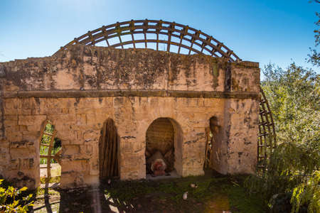 Ancient stone mill with wooden wheel in overgrown field in sunlight in Cordoba, Spainの写真素材