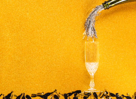 Tinsel pouring from bottle simulating Champagne in two glasses on golden glittering backgroundの写真素材