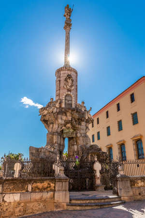 From below show of San Rafael Arcangel column with statue on top placed behind fence under blue sky in Cordoba, Spainのeditorial素材